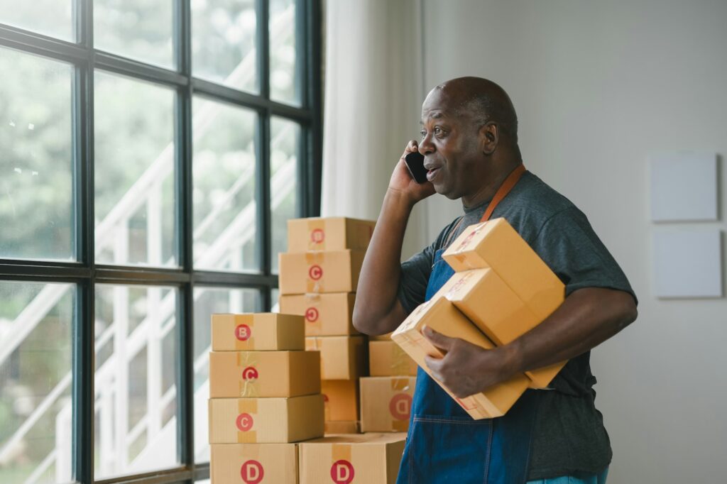 Man in an apron holding parcels and talking on the phone by the window.
